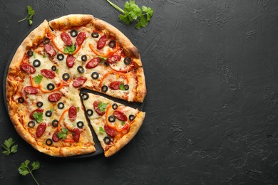 Photo of Tasty pizza with dry smoked sausages, olives, pepper and parsley on black table, top view. Space for text