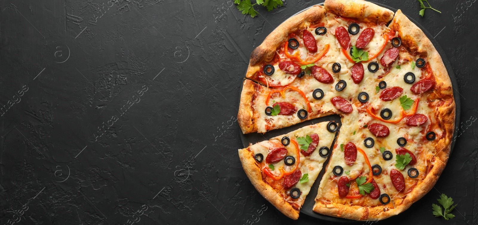 Photo of Tasty pizza with dry smoked sausages, olives, pepper and parsley on black table, top view. Space for text