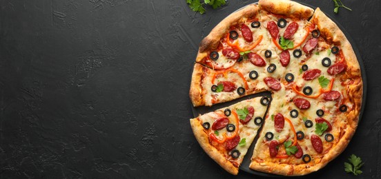 Photo of Tasty pizza with dry smoked sausages, olives, pepper and parsley on black table, top view. Space for text