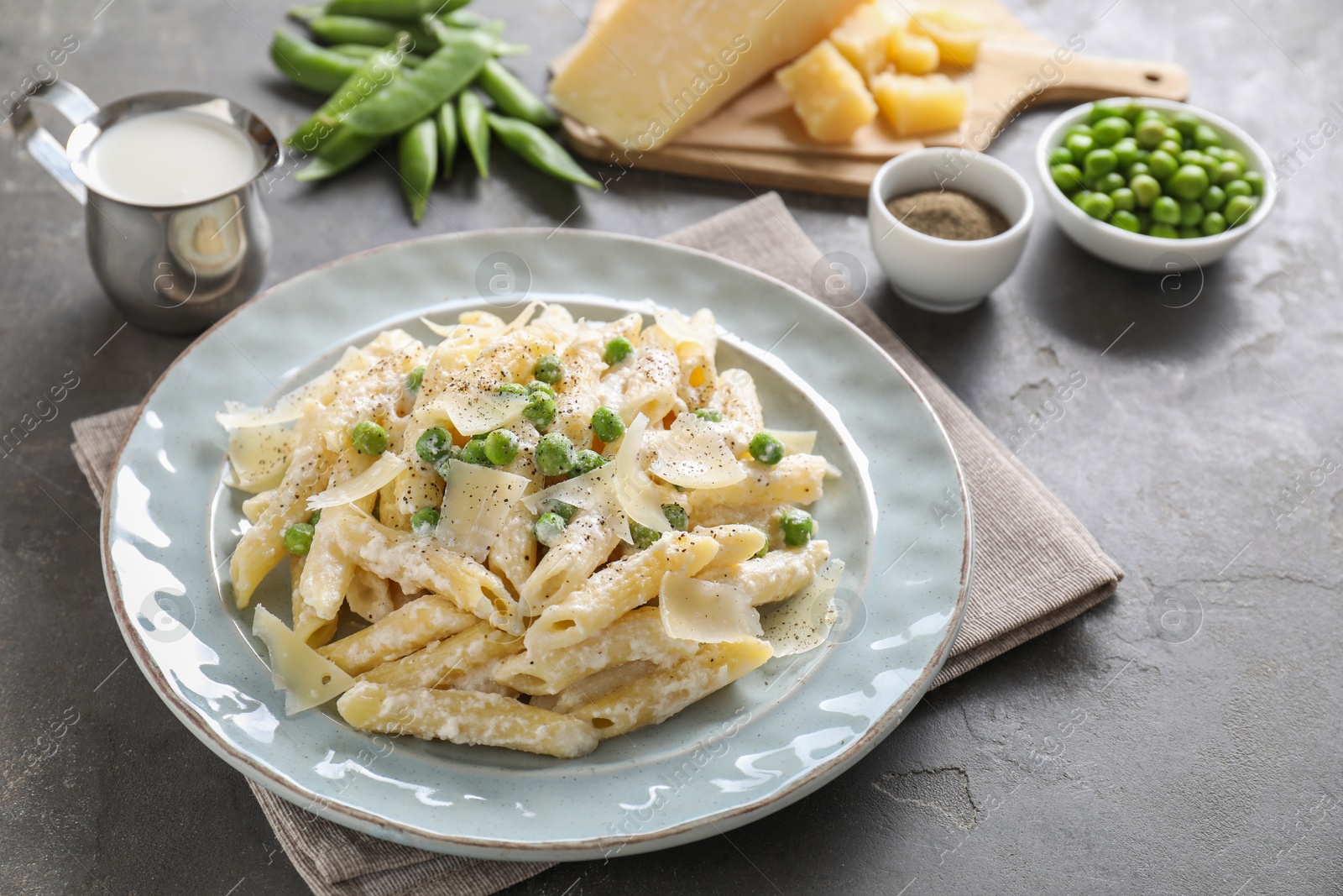 Photo of Delicious pasta with green peas, cheese, creamy sauce and ground pepper on grey table