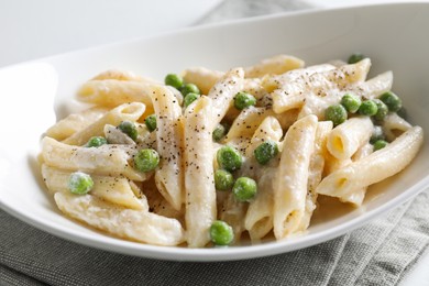 Photo of Delicious pasta with green peas and creamy sauce in bowl on table, closeup