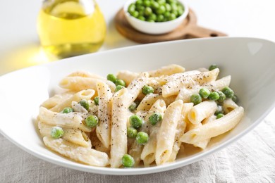 Delicious pasta with green peas and creamy sauce in bowl on table, closeup