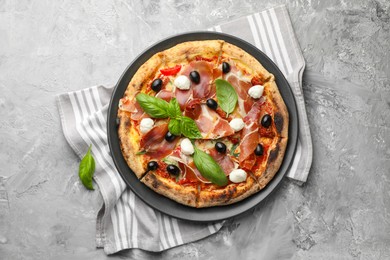 Photo of Tasty pizza with cured ham, olives, mozzarella cheese, sun-dried tomato and basil on gray textured table, top view