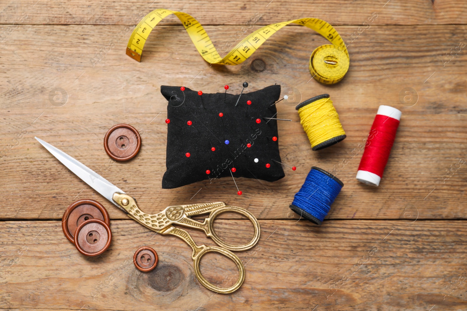 Photo of Blue pincushion with pins and other sewing tools on wooden table, flat lay