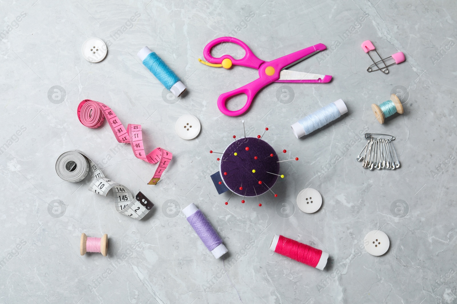 Photo of Blue pincushion with pins and other sewing tools on grey table, flat lay