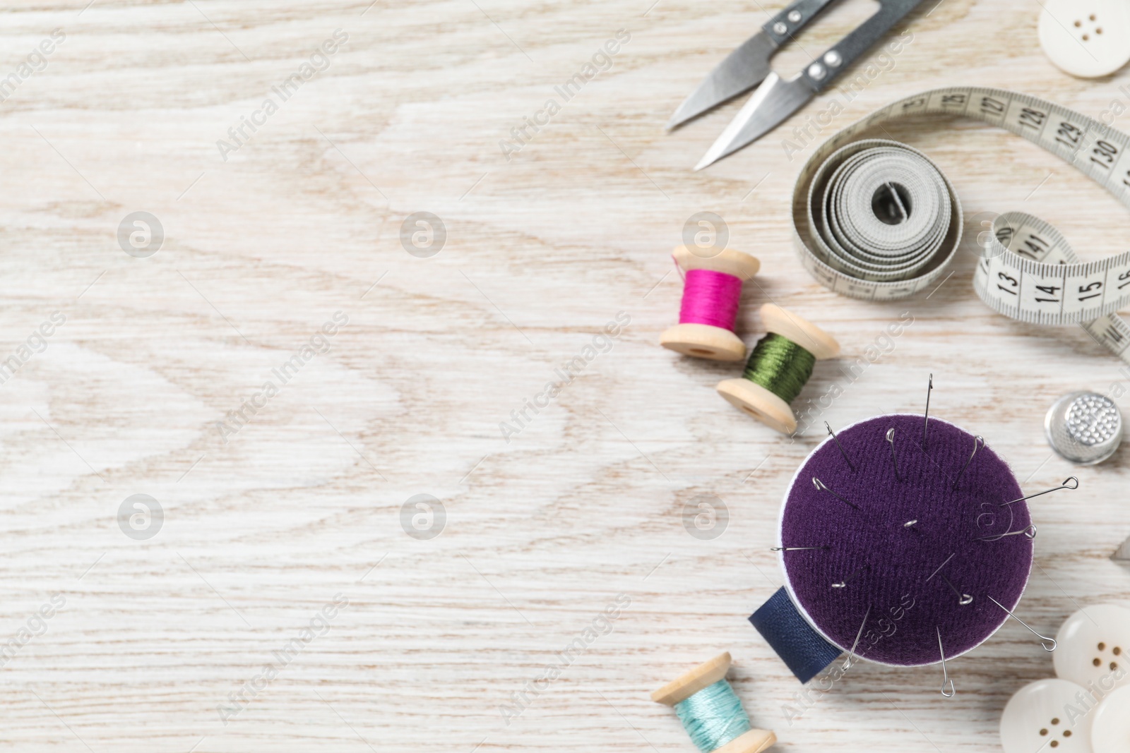 Photo of Blue pincushion with pins and other sewing tools on light wooden table, flat lay. Space for text