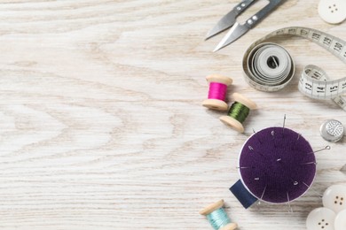 Blue pincushion with pins and other sewing tools on light wooden table, flat lay. Space for text