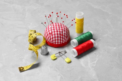 Photo of Checkered pincushion with pins and other sewing tools on grey table