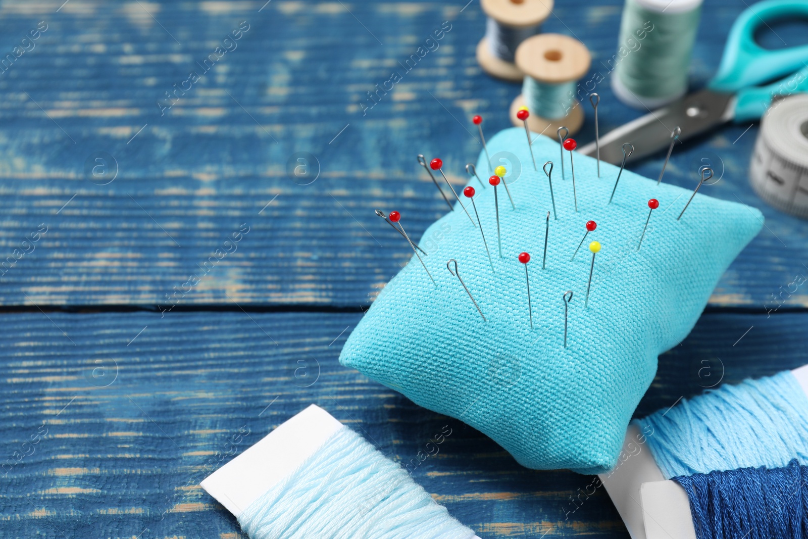 Photo of Pincushion with pins and other sewing tools on blue wooden table. Space for text