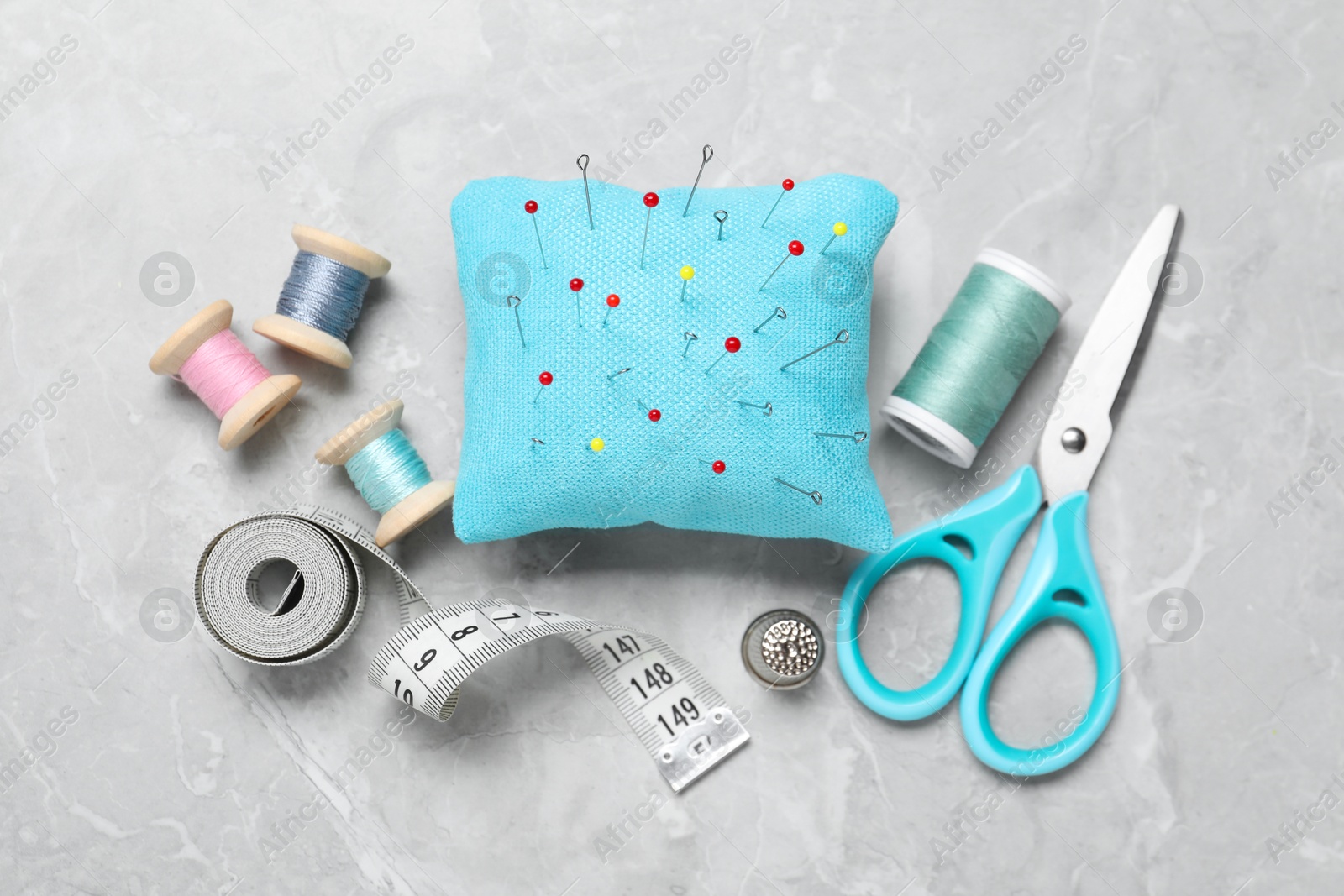 Photo of Light blue pincushion with pins and other sewing tools on grey table, flat lay