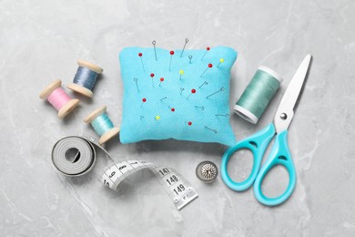 Light blue pincushion with pins and other sewing tools on grey table, flat lay