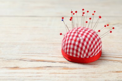 Photo of Checkered pincushion with sewing pins on light wooden table. Space for text