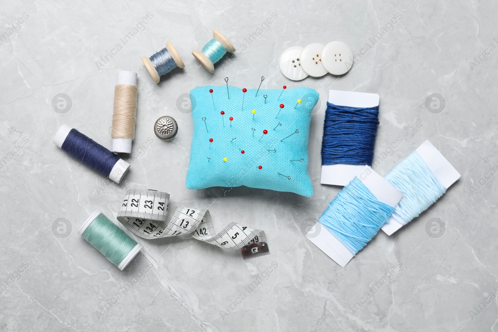 Photo of Light blue pincushion with pins and other sewing tools on grey table, flat lay