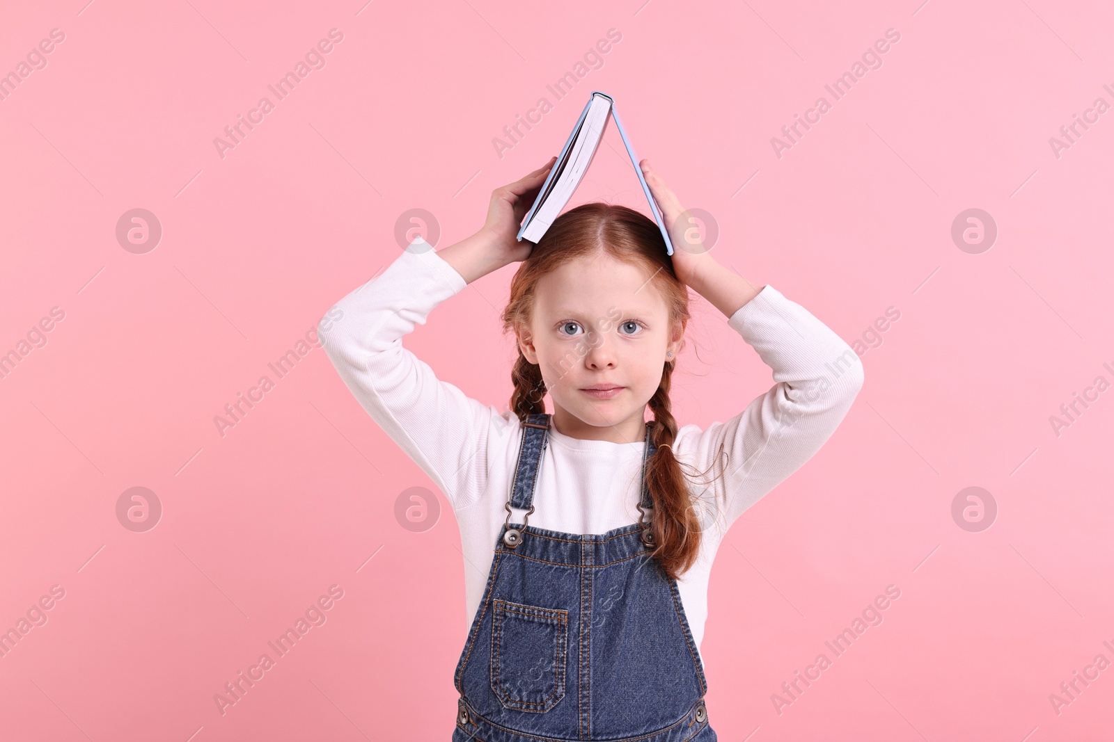 Photo of Cute little girl with book on pink background