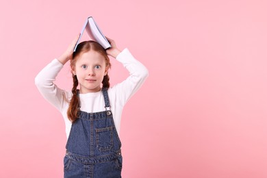 Photo of Funny little girl with book on pink background. Space for text