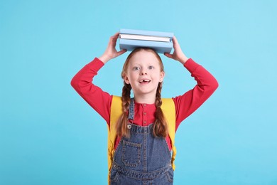 Photo of Smiling little girl with stack of books on light blue background