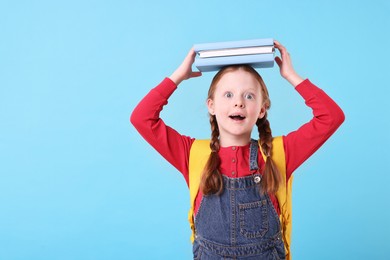 Photo of Happy little girl with stack of books on light blue background. Space for text