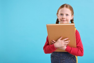 Photo of Cute little girl with book on light blue background. Space for text