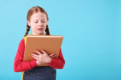 Photo of Cute little girl with book on light blue background. Space for text