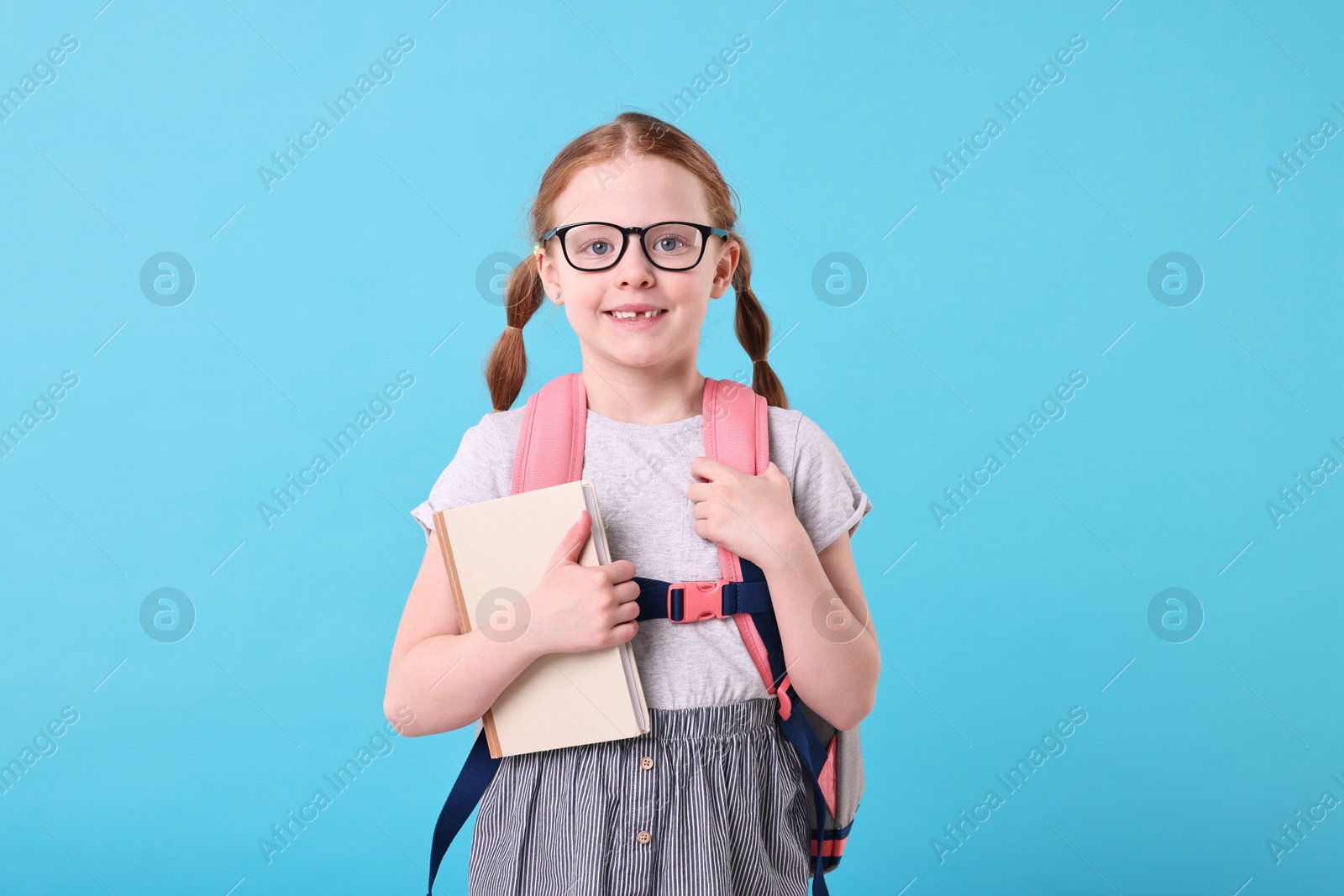 Photo of Smiling girl with book and backpack on light blue background