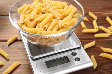 Photo of Kitchen scale with bowl of pasta on wooden table, closeup