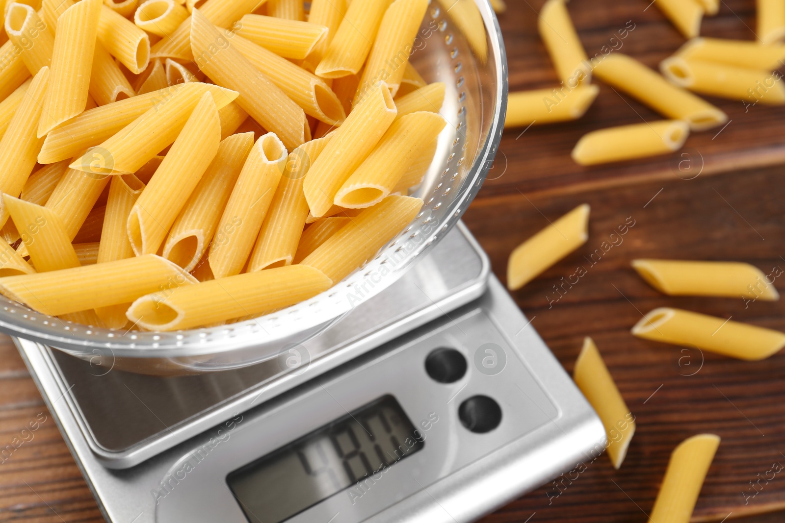 Photo of Kitchen scale with bowl of pasta on wooden table, closeup