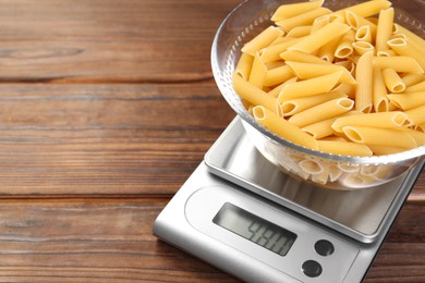 Photo of Kitchen scale with bowl of pasta on wooden table, closeup. Space for text