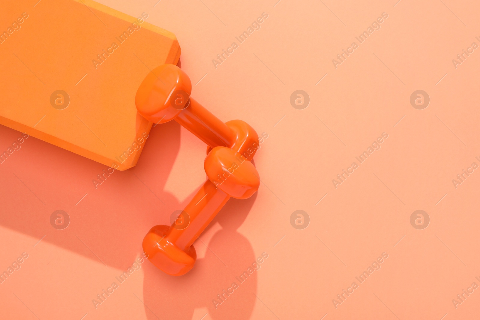 Photo of Dumbbells and yoga block on coral background, flat lay. Space for text