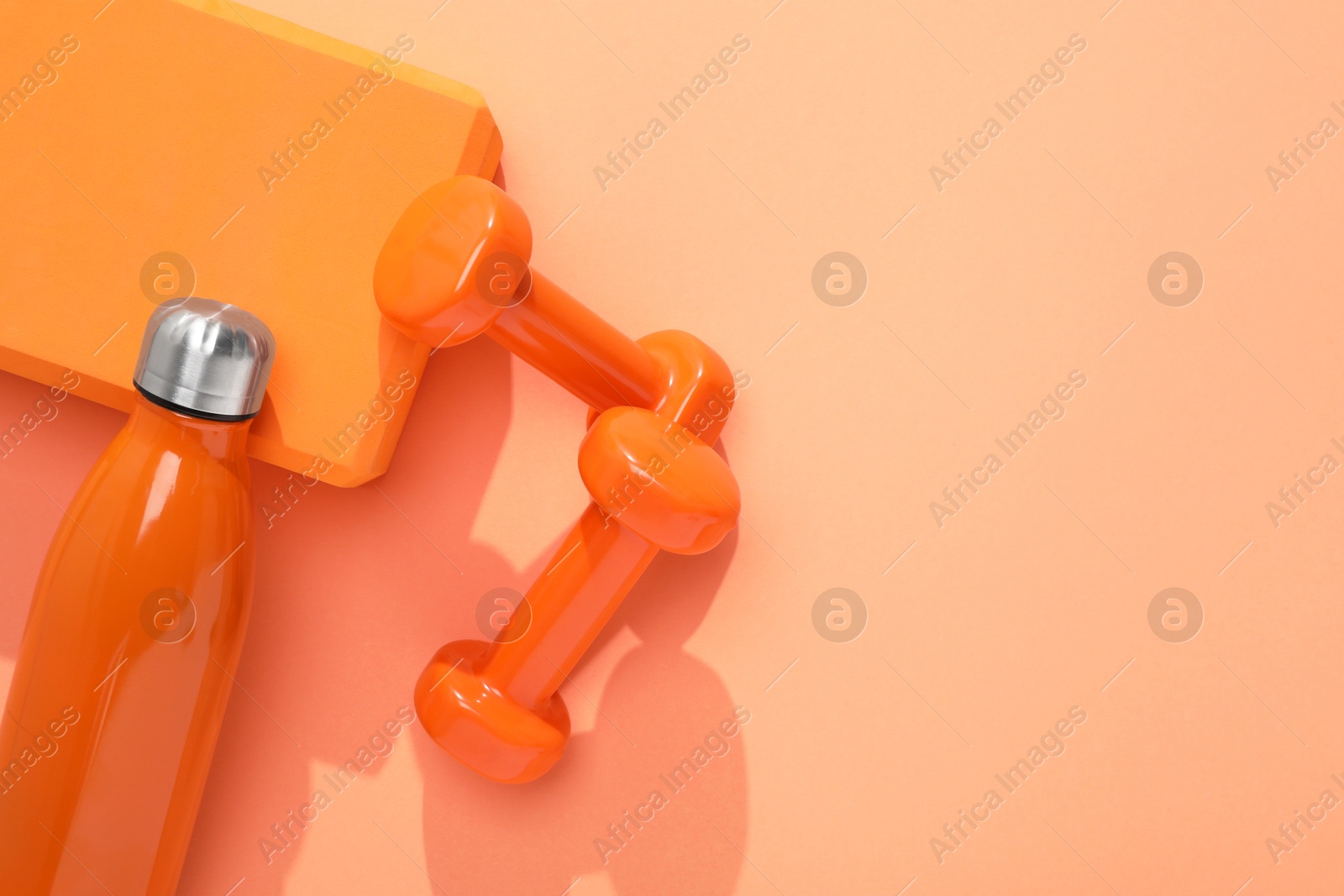 Photo of Dumbbells, thermo bottle and yoga block on coral background, flat lay. Space for text