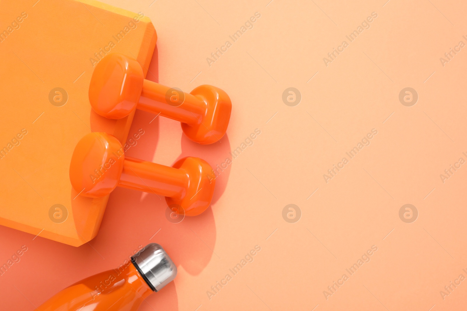 Photo of Dumbbells, thermo bottle and yoga block on coral background, flat lay. Space for text