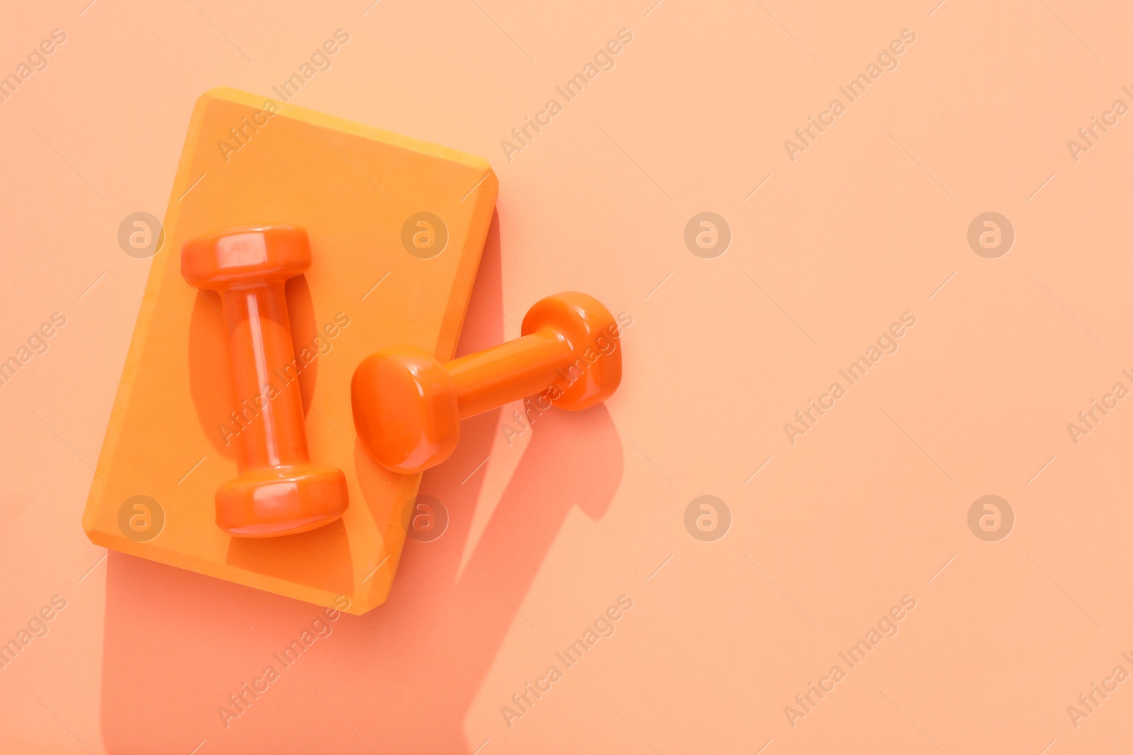 Photo of Dumbbells and yoga block on coral background, flat lay. Space for text