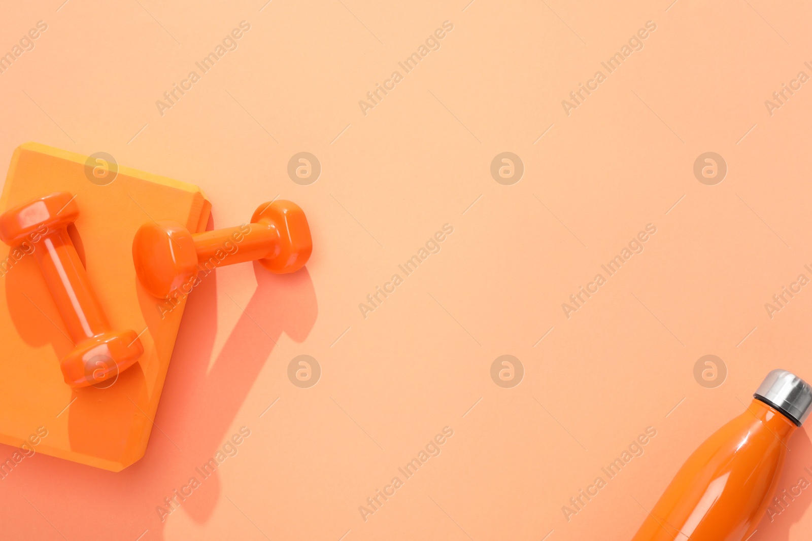 Photo of Dumbbells, thermo bottle and yoga block on coral background, flat lay. Space for text