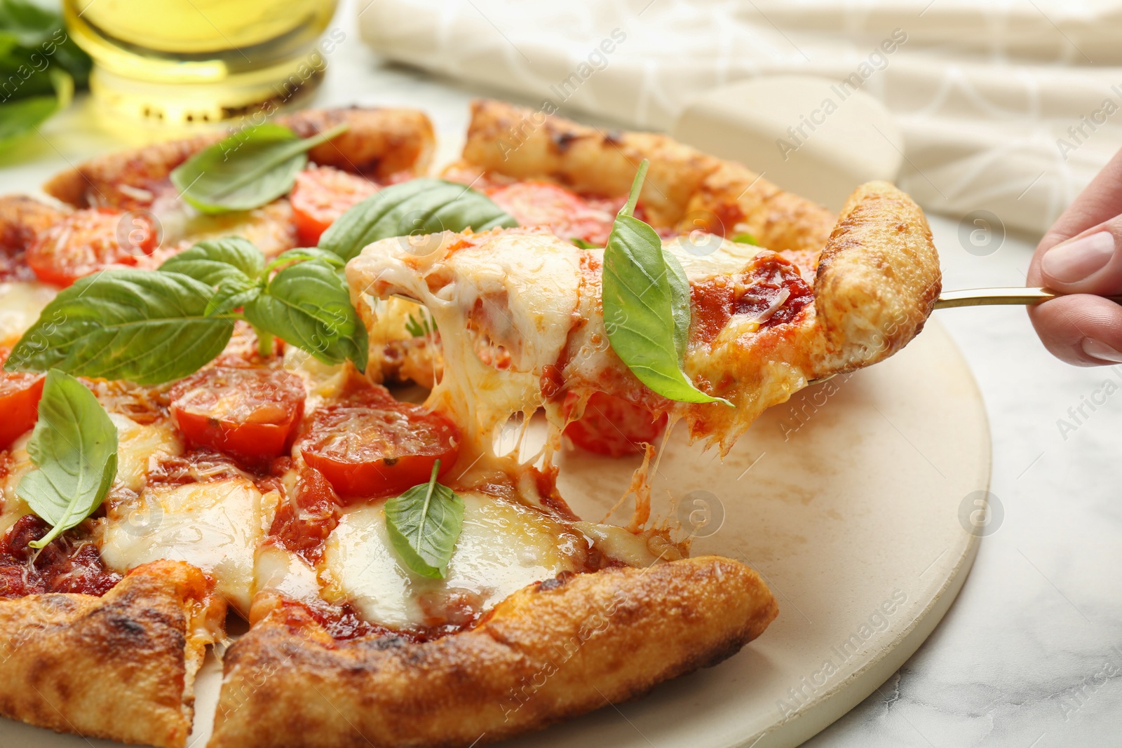 Photo of Woman taking piece of delicious Margherita pizza at white marble table, closeup