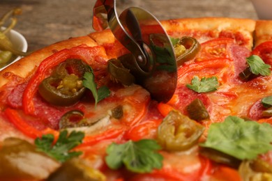 Photo of Cutting delicious pizza Diablo at table, closeup