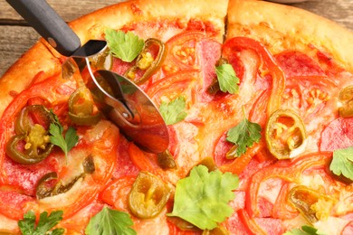 Photo of Cutting delicious pizza Diablo at table, closeup