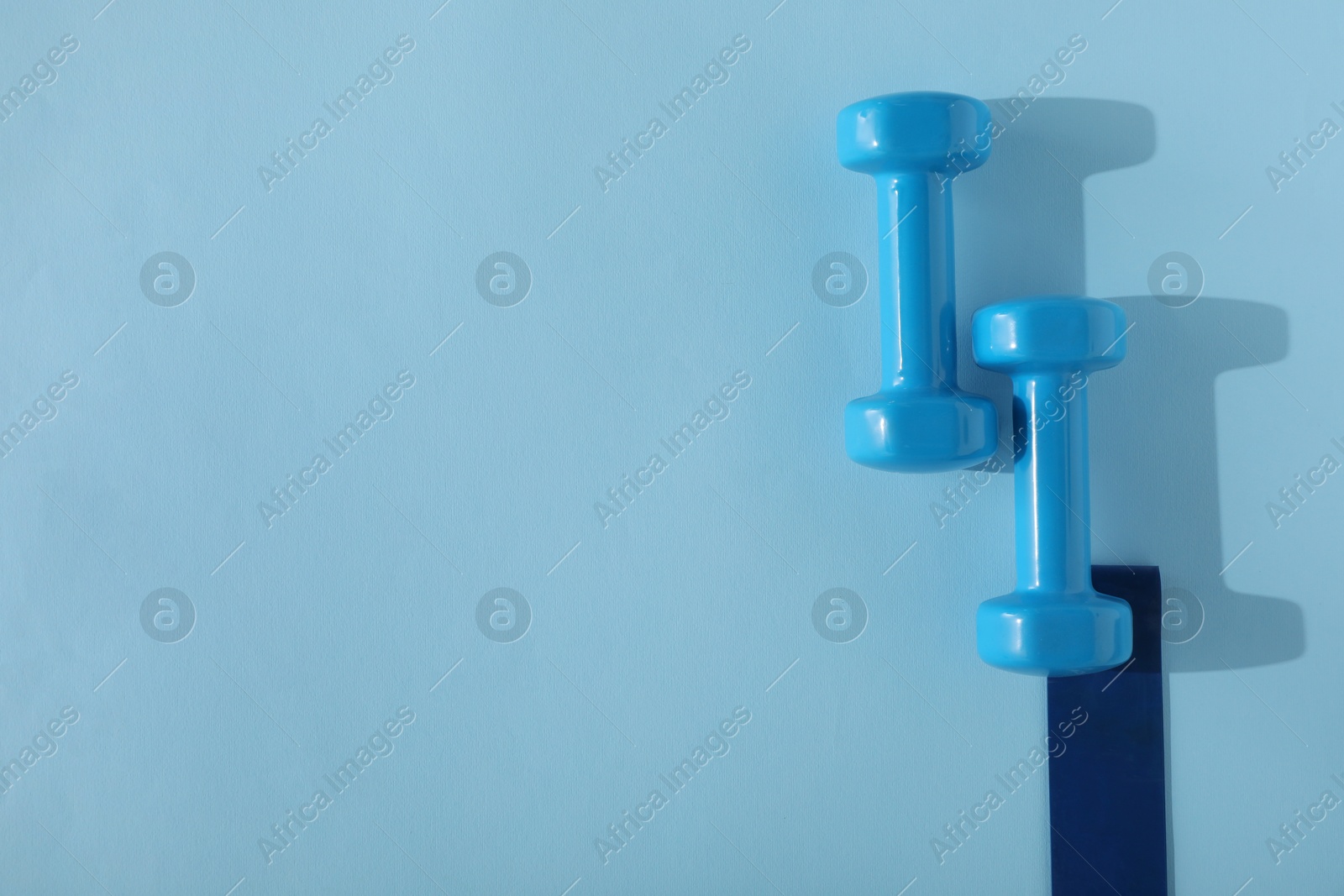 Photo of Two dumbbells and fitness elastic band on light blue background, flat lay. Space for text