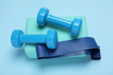 Photo of Two dumbbells, yoga block and fitness elastic band on light blue background, above view