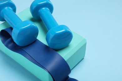 Photo of Two dumbbells, yoga block and fitness elastic band on light blue background, closeup. Space for text