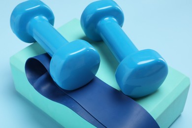 Photo of Two dumbbells, yoga block and fitness elastic band on light blue background, closeup