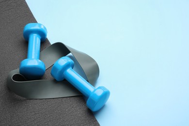 Photo of Two dumbbells, yoga mat and fitness elastic band on light blue background. Space for text