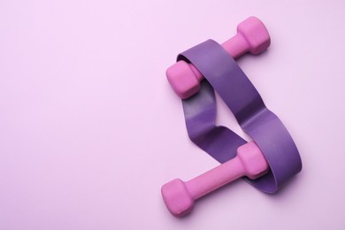 Photo of Two dumbbells and fitness elastic band on violet background, top view. Space for text