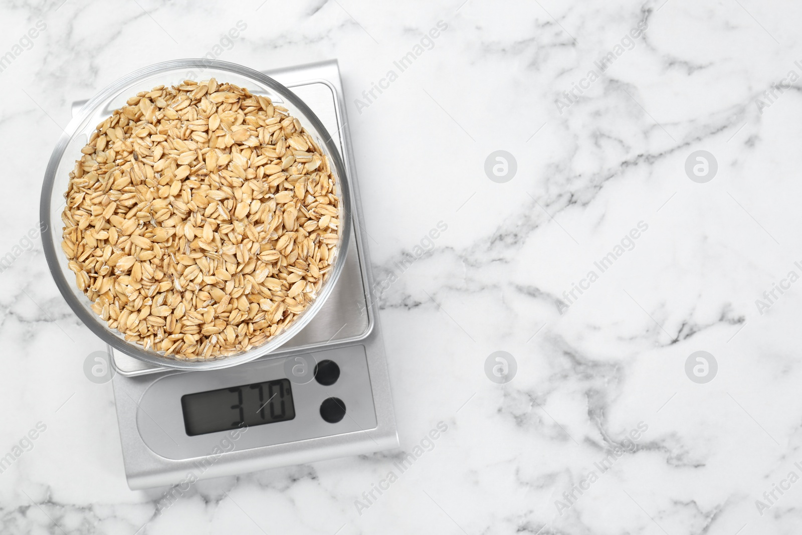 Photo of Kitchen scale with bowl of dry oats on white marble table, top view. Space for text