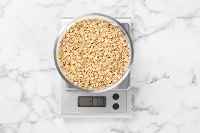 Photo of Kitchen scale with bowl of dry oats on white marble table, top view