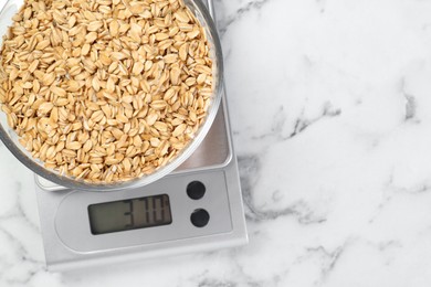 Photo of Kitchen scale with bowl of dry oats on white marble table, top view. Space for text