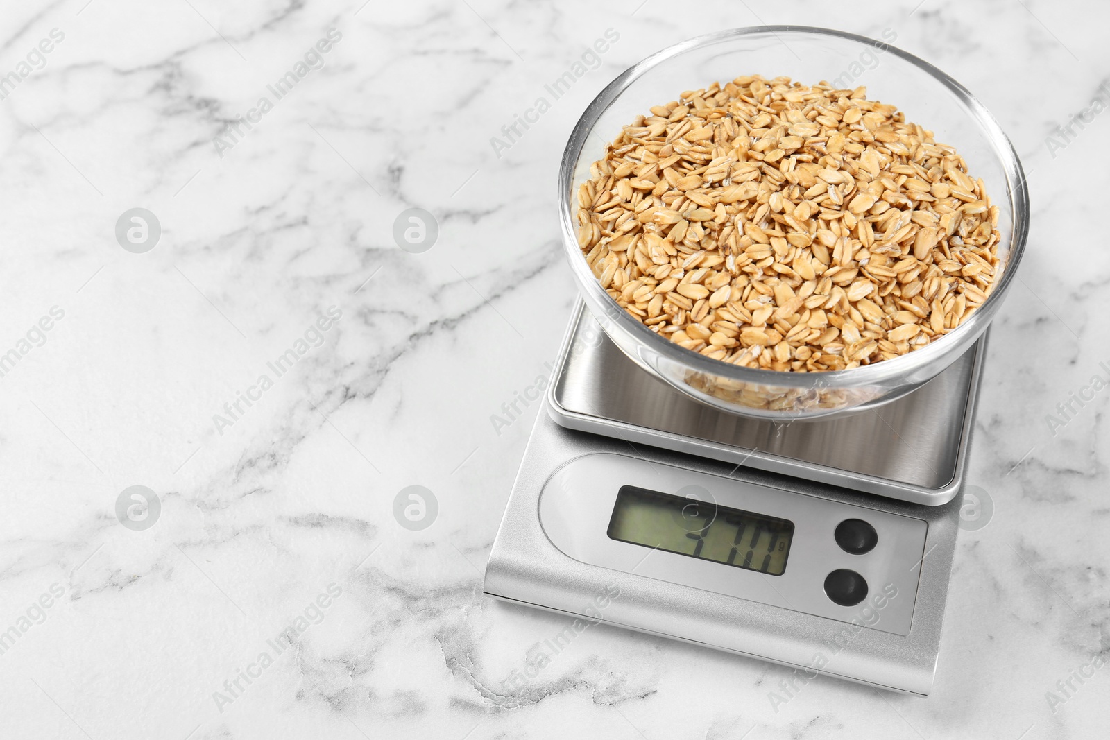 Photo of Kitchen scale with bowl of dry oats on white marble table. Space for text