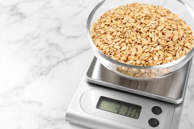 Photo of Kitchen scale with bowl of dry oats on white marble table, closeup. Space for text