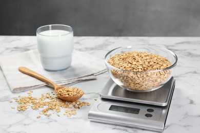 Photo of Kitchen scale with bowl of dry oats, milk and spoon on white marble table