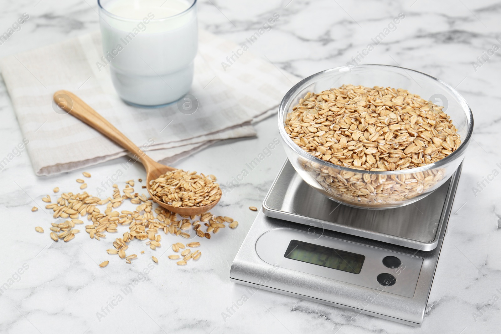 Photo of Kitchen scale with bowl of dry oats, milk and spoon on white marble table