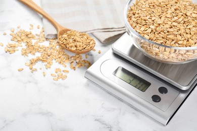 Kitchen scale with bowl of dry oats and spoon on white marble table, closeup