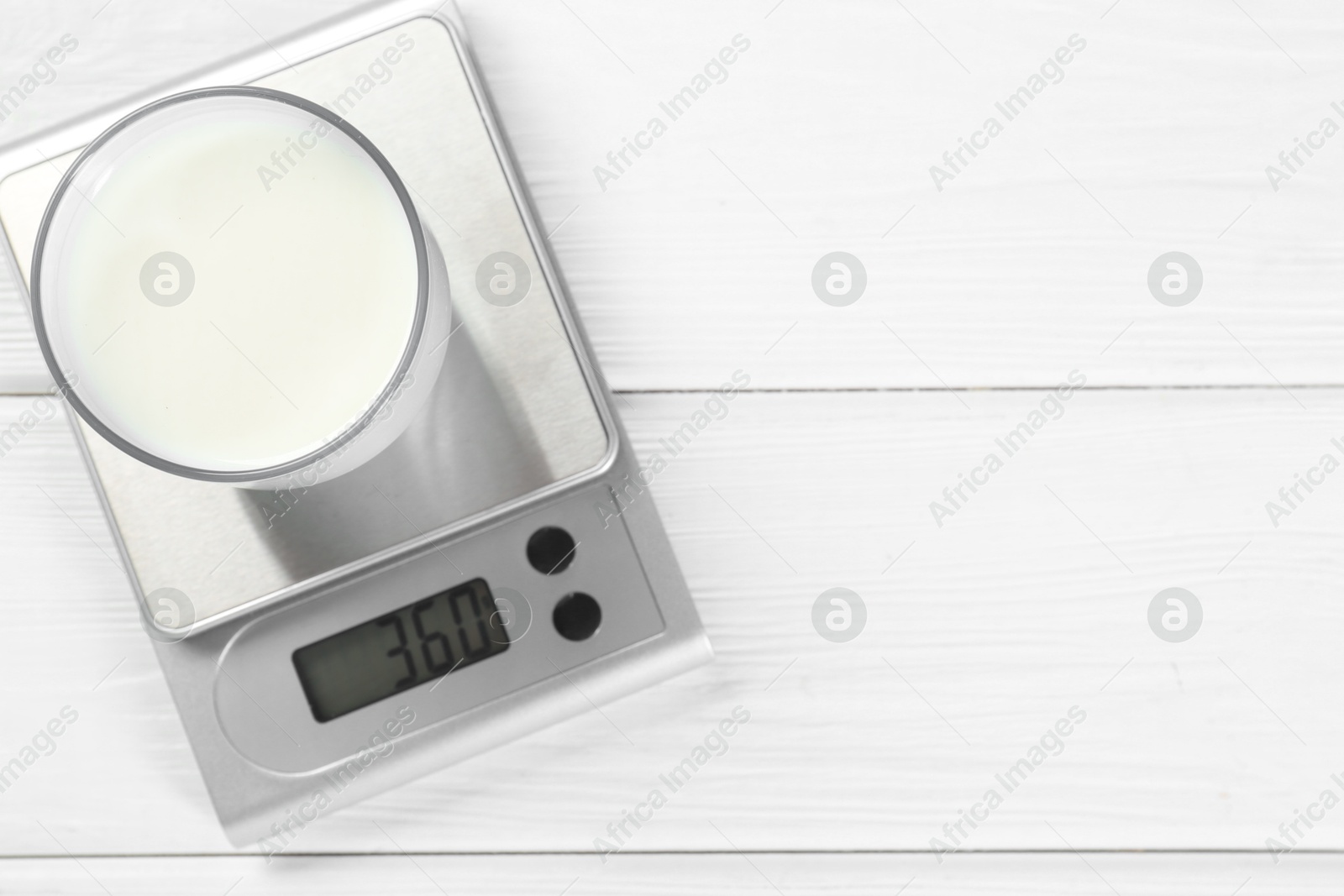 Photo of Kitchen scale with glass of milk on white wooden table, top view. Space for text